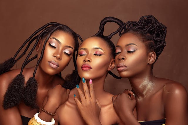 Three beautiful Black African women wearing beautiful makeup colors, nail colors, and traditional African hairstyles.